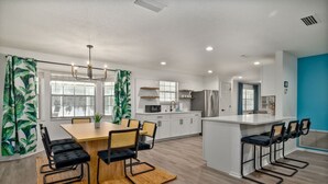 Une cuisine moderne avec des meubles blancs, un îlot central et un coin repas comprenant une table et des chaises en bois.