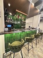 Una zona de bar con un revoque de azulejos verdes, una caja registradora y taburetes de bar.