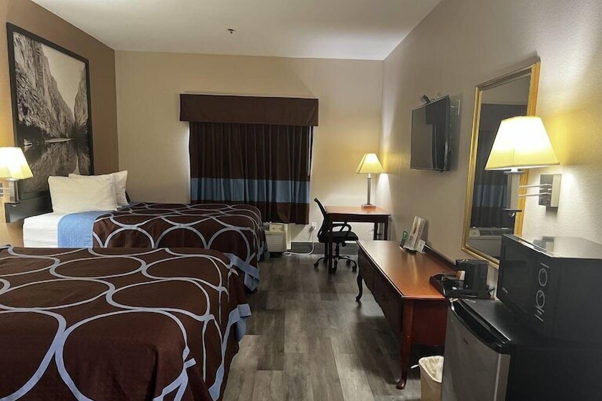 Ein Hotelzimmer mit zwei Betten, einem Schreibtisch, einem Sessel, einem Fernseher und einem Badezimmer.