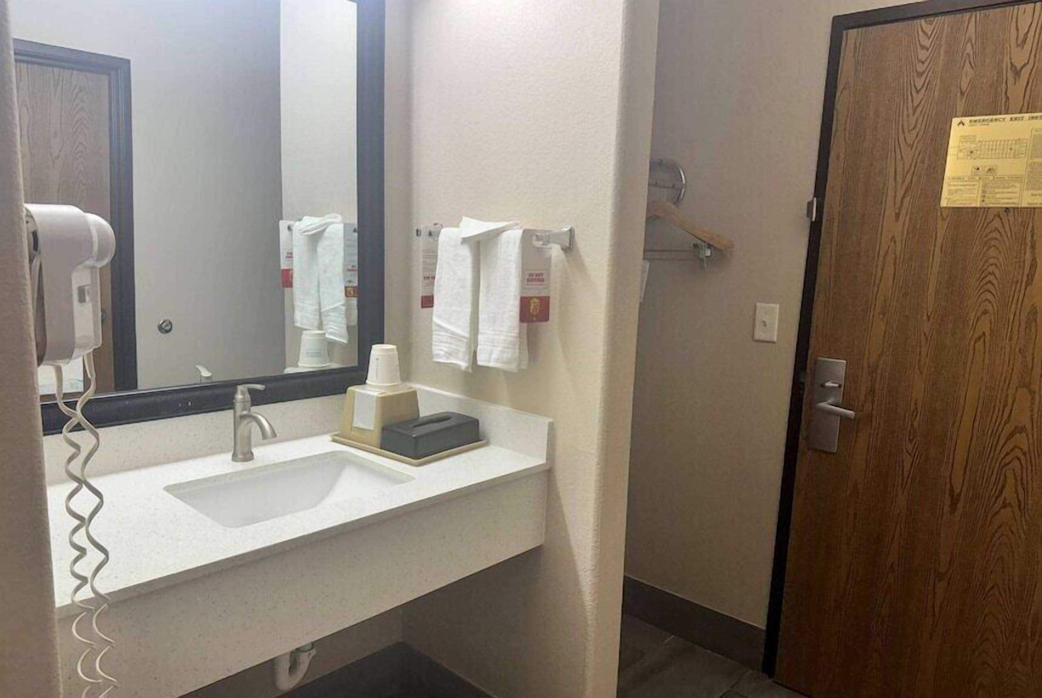 A bathroom with a sink, mirror, towel rack, and a door with a notice.