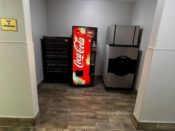 Un área de venta con una máquina expendedora de hielo y bebidas, una máquina expendedora de Coca-Cola y un refrigerador.
