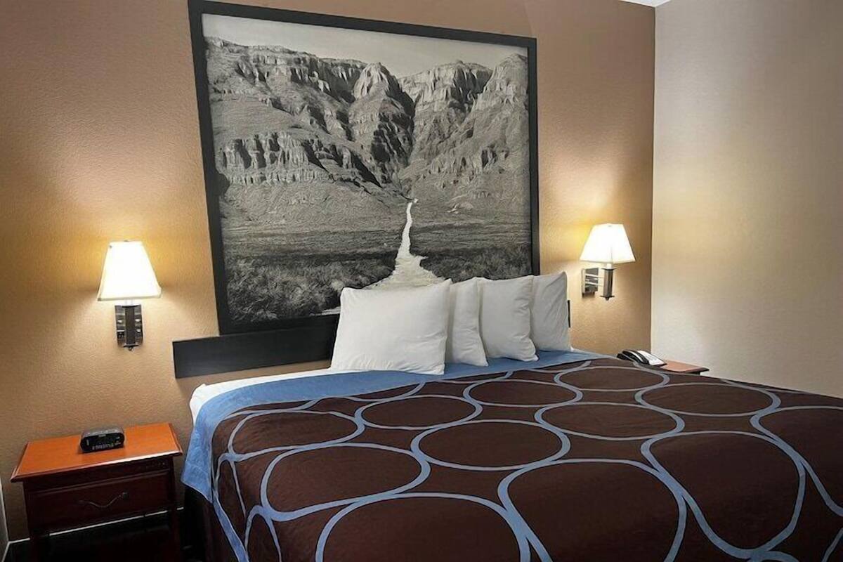 Ein Hotelzimmer mit einem großen Bett, zwei Nachttischlampen, einem Nachttisch mit Radio und einem Wandbild von einer Berglandschaft.
