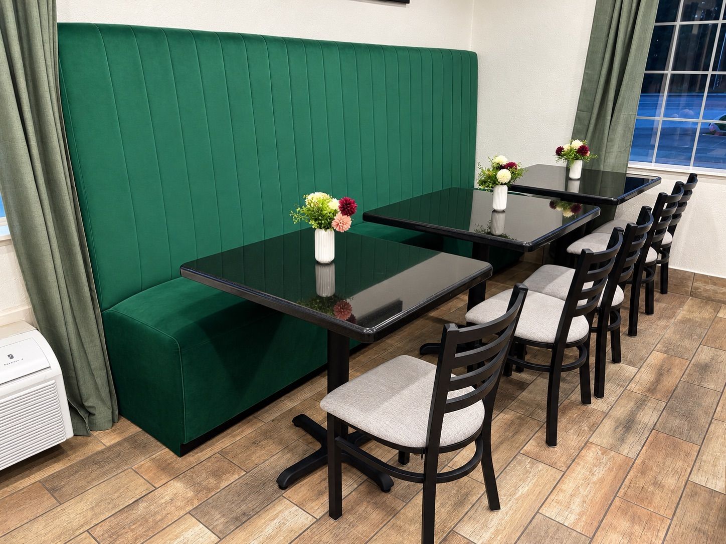 Un espace repas comprenant un coin salon avec des banquettes recouvertes d’un tissu vert, une table à plateau en verre et six chaises.