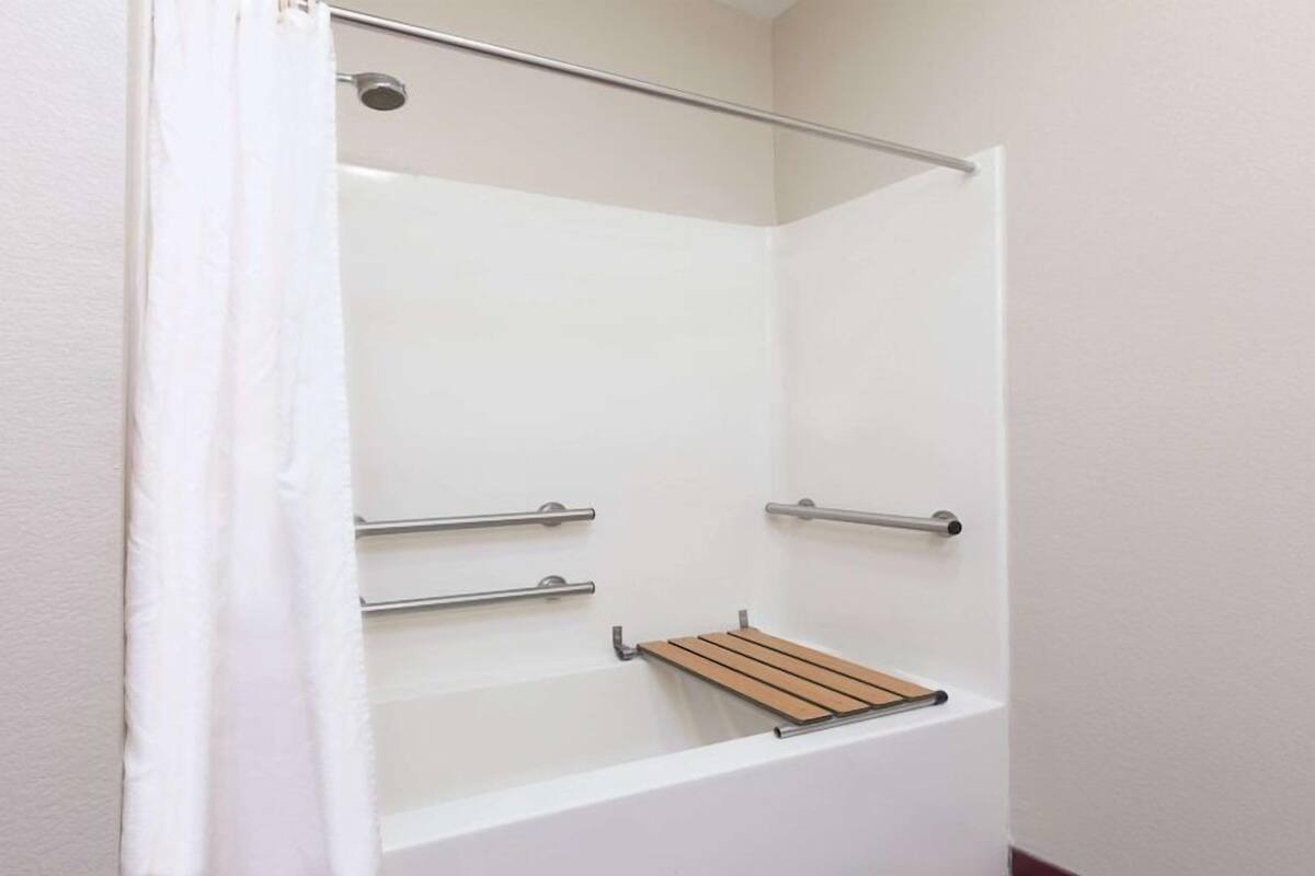 Eine Dusche mit weißem Vorhang, einem Holzregal und Metallhandläufen.