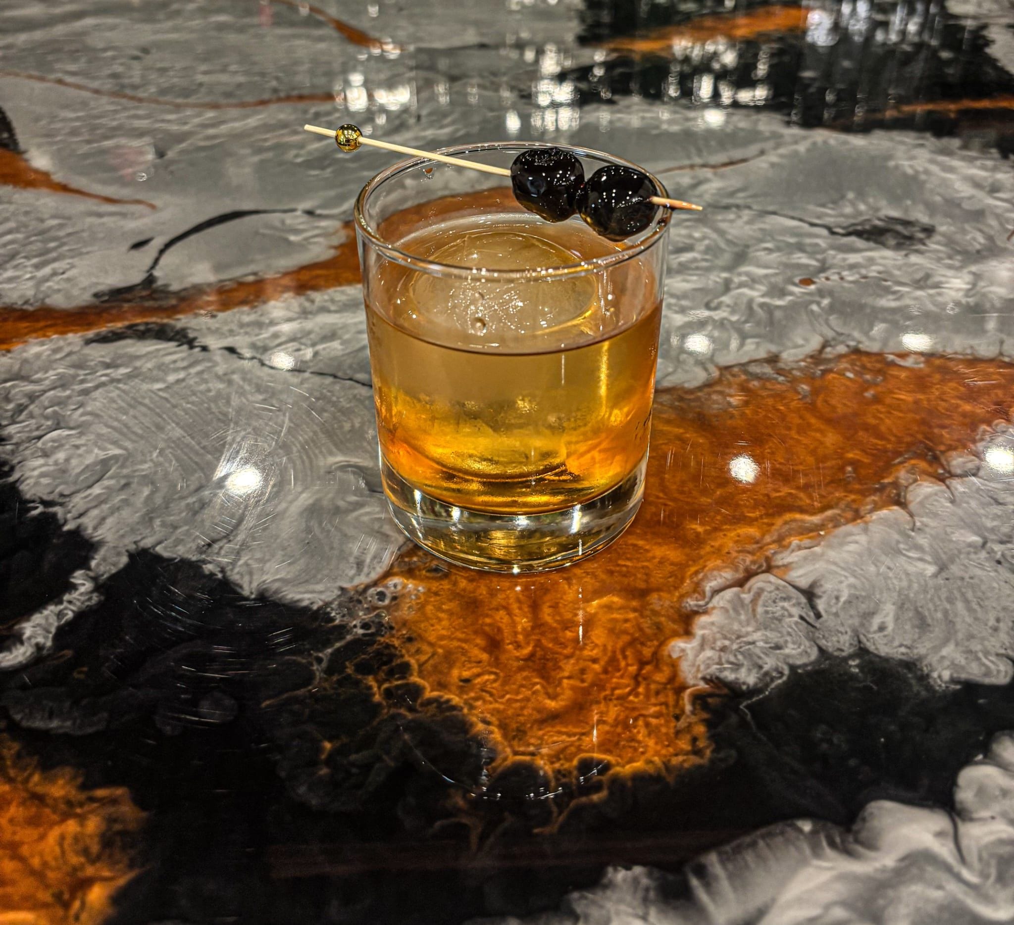 A glass of amber-colored liquid with a garnish on a reflective surface.