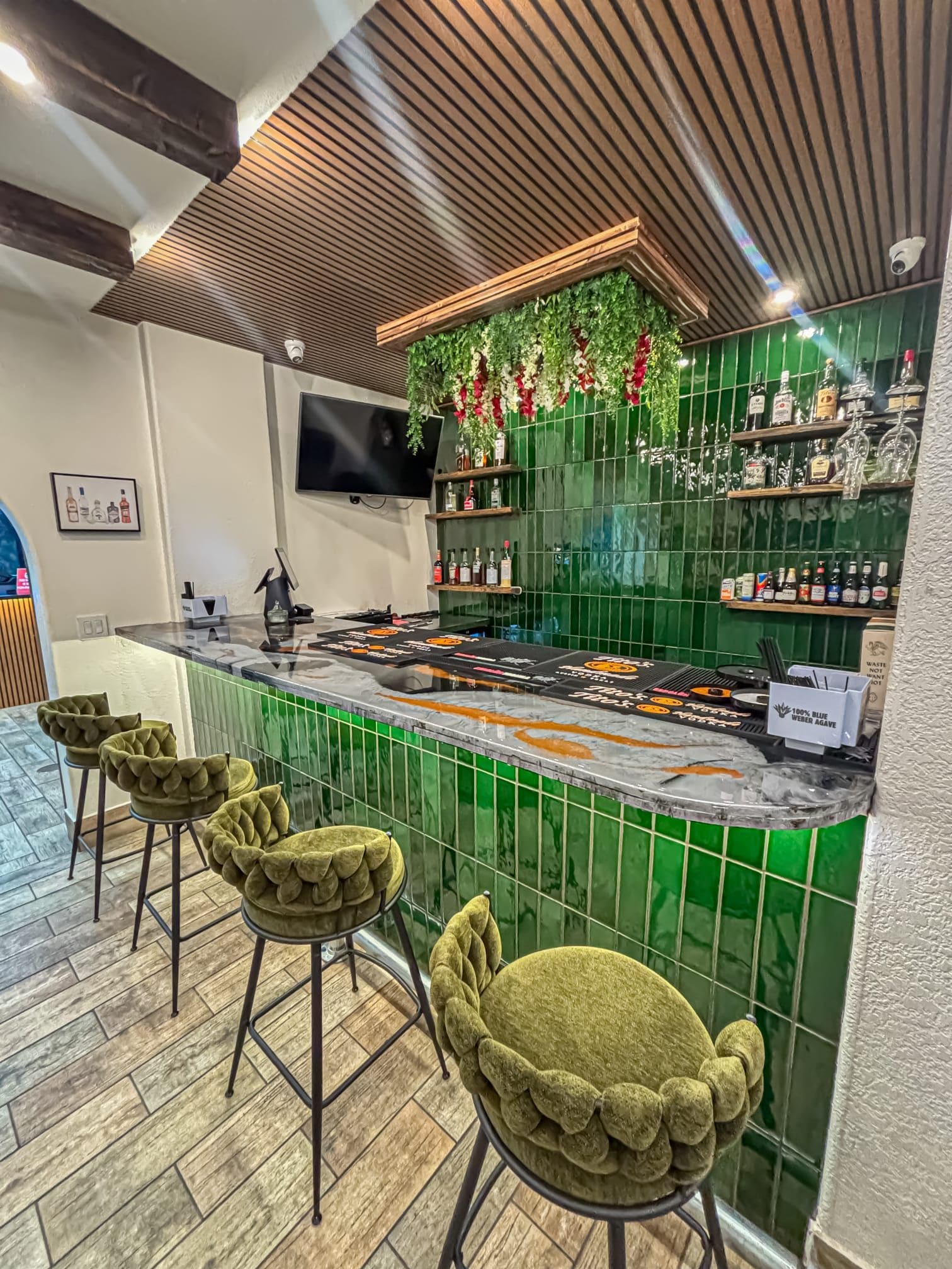 A bar area with a green tiled backsplash, a flat-screen TV, and a variety of liquor bottles.