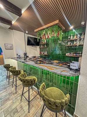 A bar area with a green tiled backsplash, a flat-screen TV, and a variety of liquor bottles. - Hotel Piney Woods (Huntsville)