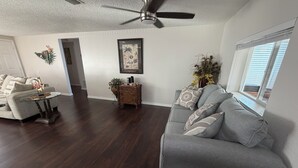 A spacious living room with a grey sofa, a glass coffee table, and a dark wooden floor. - Family 2BR Oasis w/Private Pool & HDTV, PAWsitive (Port Richey)