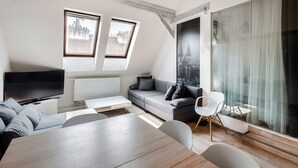Uma sala de estar moderna com sofá, TV e mesa de jantar. Há duas janelas com vista para a cidade e uma janela grande com cortinas.