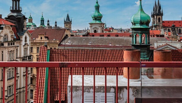 Vista de uma paisagem urbana com edifícios históricos e torres verdejantes em forma de cúpula.