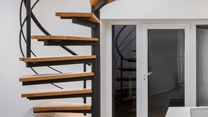 Uma escada espiral moderna com degraus de madeira e guarda-corpo de metal preto, que dá acesso a uma porta de vidro.