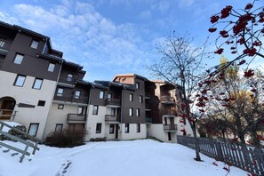 Un edificio residencial de varios pisos con balcones, suelo cubierto de nieve y cielo despejado.
