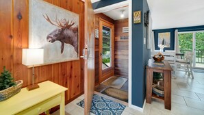 Un interior de madera con un cuadro de alce, una puerta que da al exterior y vistas del paisaje.