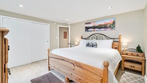 Un dormitorio con cama de madera, mesita de noche, cómoda, un cuadro en la pared y una puerta.