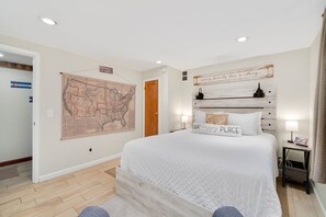 A bedroom with a large bed, a map on the wall, a wooden headboard, and a nightstand with a lamp.