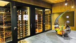 Uma adega com várias prateleiras de garrafas de vinho, uma grande escultura metálica decorativa e um chão de mármore.