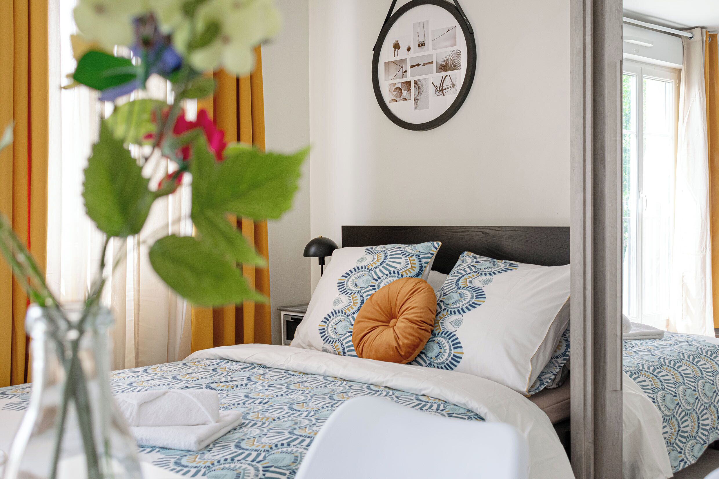 Una cama bien hecha con ropa de cama estampada, una mesita de noche con lámpara y un collage de fotos en la pared.