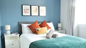 Una cama bien hecha con un edredón color turquesa, dos mesitas de noche con lámparas y cuadros en la pared.