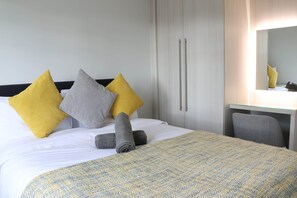 A neatly made bed with a patterned bedspread, a pair of rolled towels, and three pillows in yellow, gray, and white. - Luxury 4 Bedroom Townhouse In Stirling (Stirling)