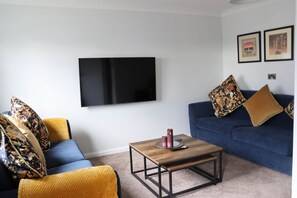 A living room with a sofa, a coffee table, a flat-screen TV, and two framed pictures on the wall. - Luxury 4 Bedroom Townhouse In Stirling (Stirling)