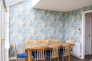 A dining area with a glass table and wooden chairs, a floral wallpaper, and a white door. - Luxury 4 Bedroom Townhouse In Stirling (Stirling)