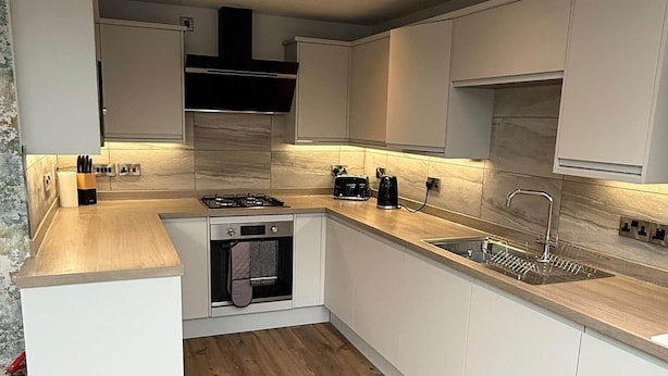 A modern kitchen with white cabinets, a wooden countertop, a built-in oven, and a sink.