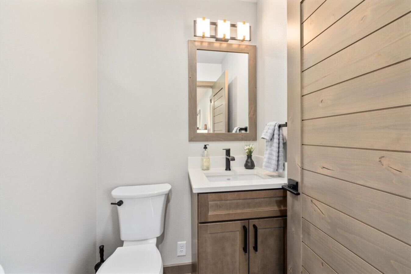 A bathroom with a toilet, a sink with a mirror above it, and wooden cabinets.