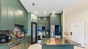 A modern kitchen with green cabinets, stainless steel appliances, and a marble countertop.