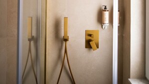 Un baño moderno con cabina de ducha de vidrio, ducha con cabezal dorado y panel de control en la pared.