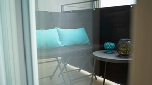Una habitación moderna con separador de vidrio, un sofá gris con cojines turquesa y una pequeña mesa redonda con objetos decorativos.