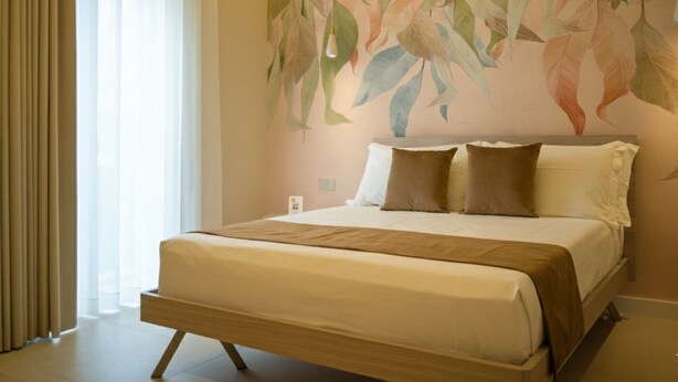 Una habitación de hotel con una cama grande, cortinas color beige y un mural en la pared.