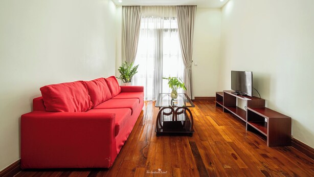 Un salon avec un canapé rouge, une table basse en verre, un téléviseur posé sur un meuble en bois et une plante sur la table.