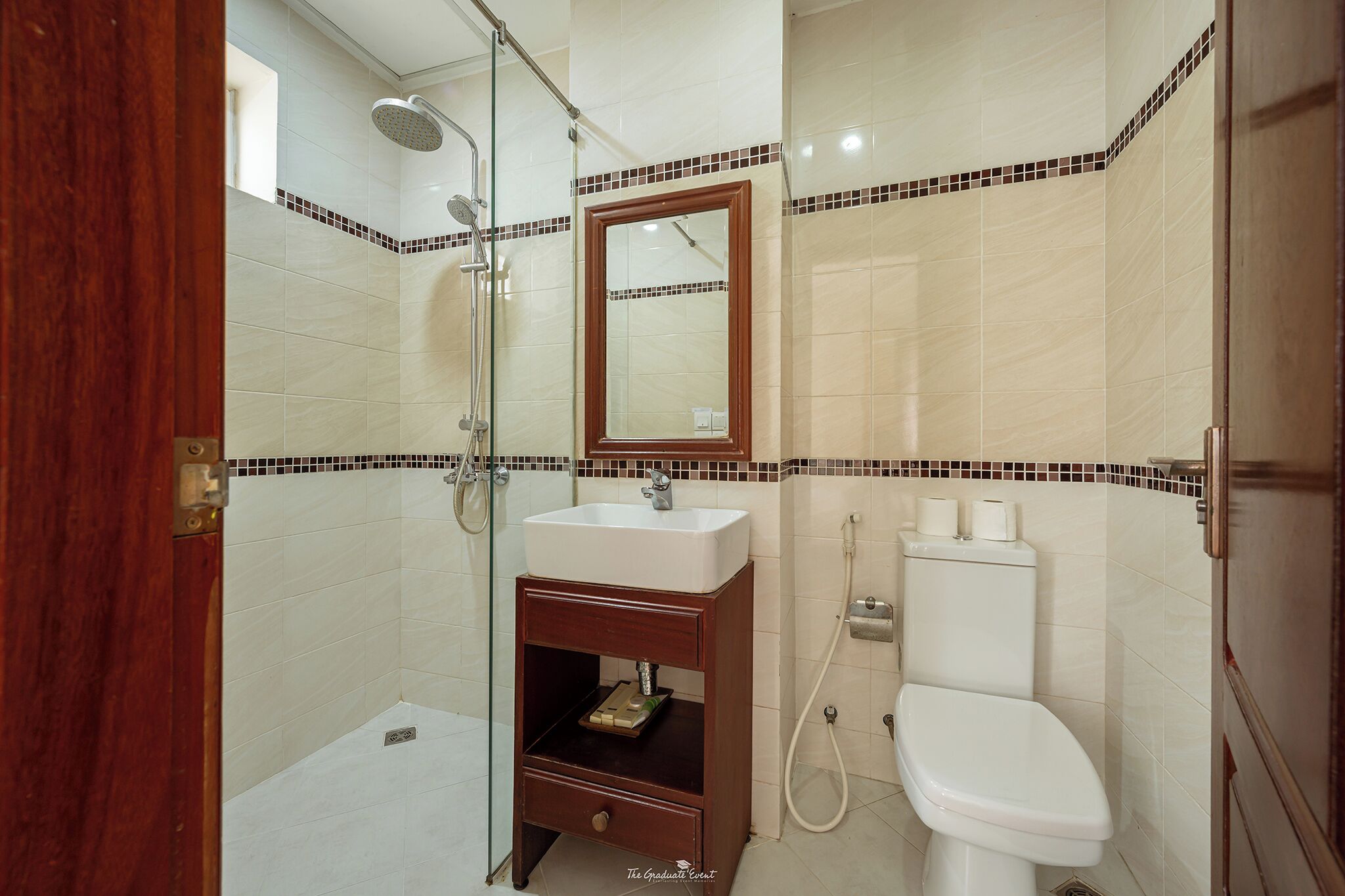 Un baño con cabina de ducha de vidrio, un lavabo blanco, un mueble de tocador de madera, un inodoro y un espejo.