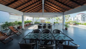Un espace extérieur abrité, aménagé avec des tables et des chaises, des plantes en pot, et offrant une vue sur les bâtiments en arrière-plan.