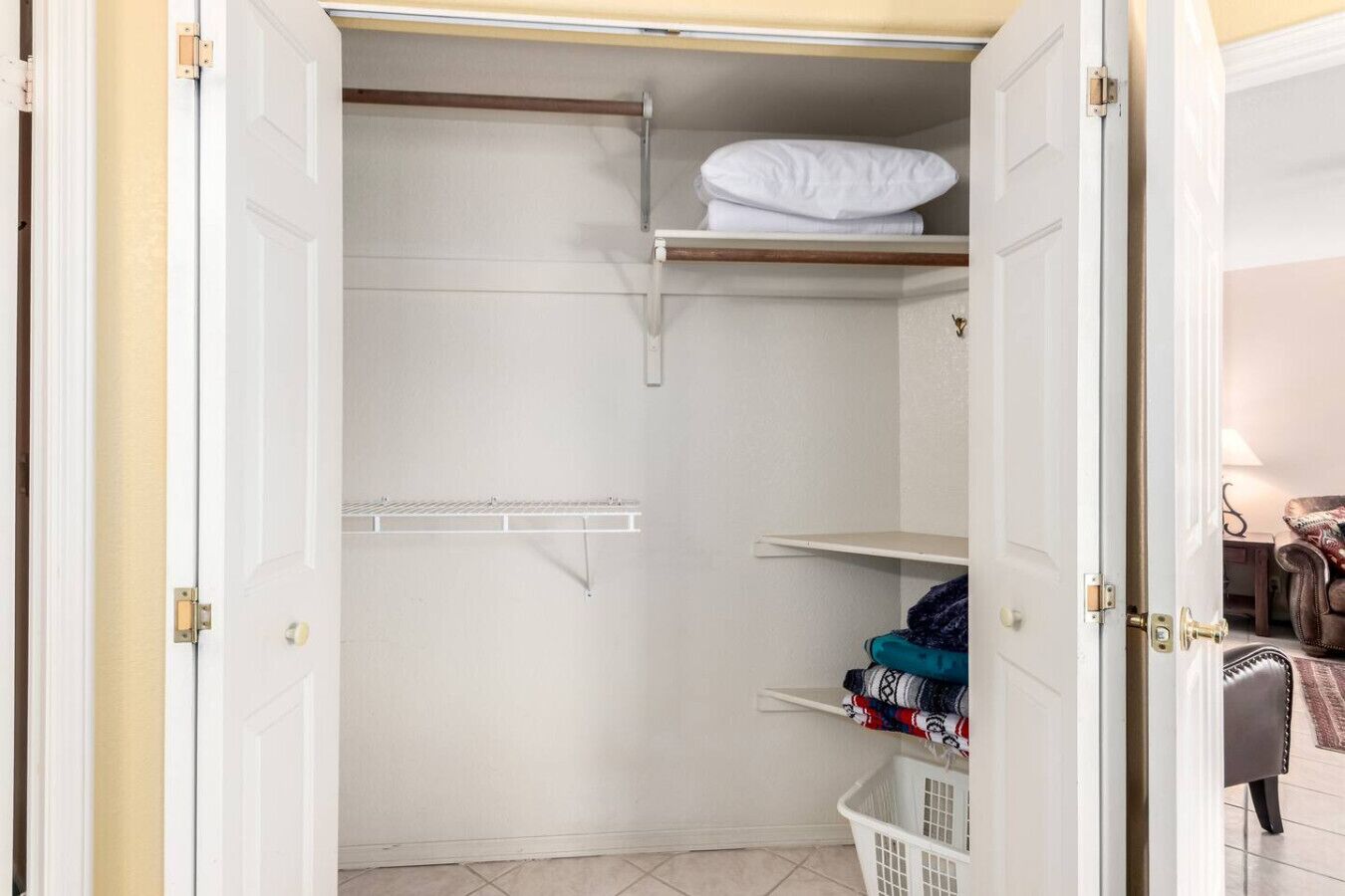 A walk-in closet with open doors, featuring a hanging rod, shelves, and a folded bed.