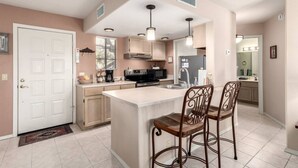 A modern kitchen with a central island, bar stools, and a microwave.