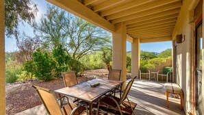 An outdoor patio with a table and chairs, surrounded by desert vegetation and a clear sky.