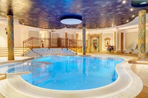A luxurious indoor swimming pool with a starry ceiling, ornate columns, and a grand staircase leading to a balcony. - Hotel Glockenstuhl (Gerlos)
