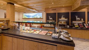 A buffet area with wooden cabinets, a glass display case, and a large screen displaying a scenic view. - Hotel Glockenstuhl (Gerlos)
