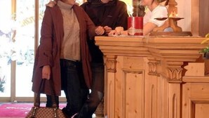 A reception area with a wooden counter, a chandelier, and a large window. - Hotel Glockenstuhl (Gerlos)
