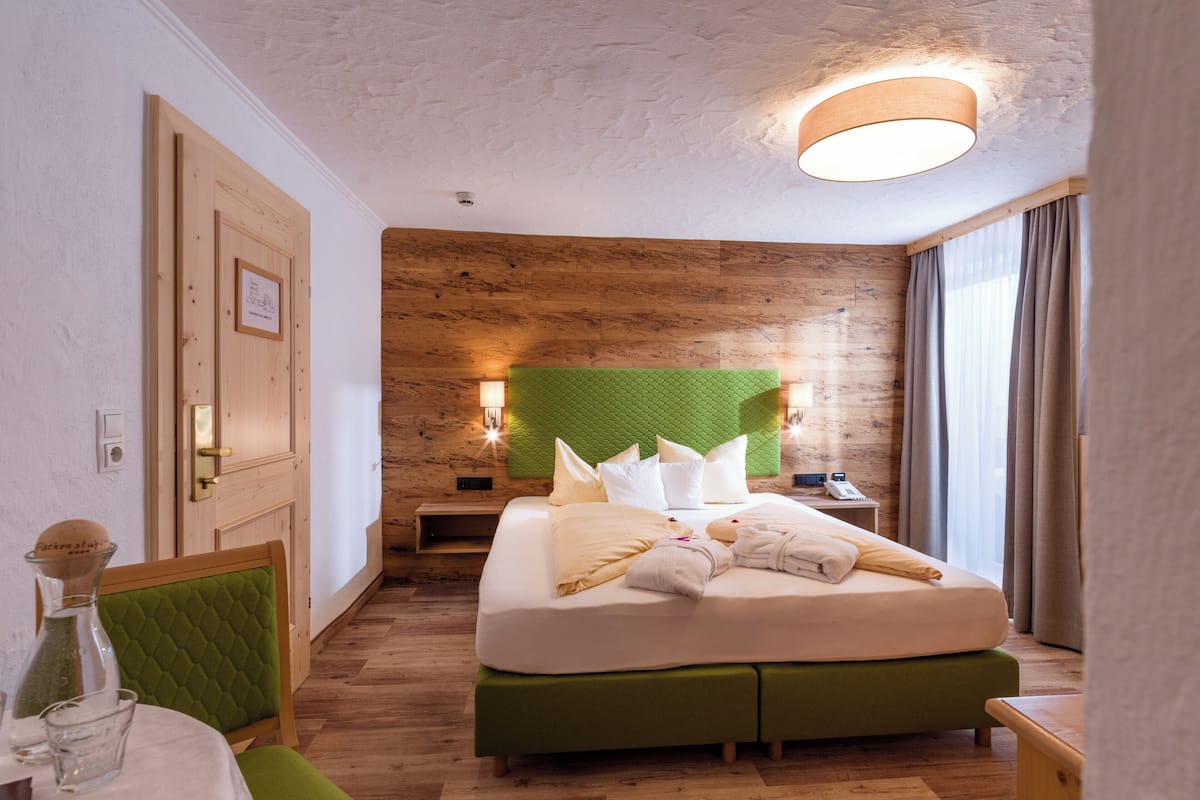 Une chambre d’hôtel avec un mur en bois, une tête de lit verte, un lit avec une literie blanche, une table de chevet, une lampe et une fenêtre avec des rideaux.