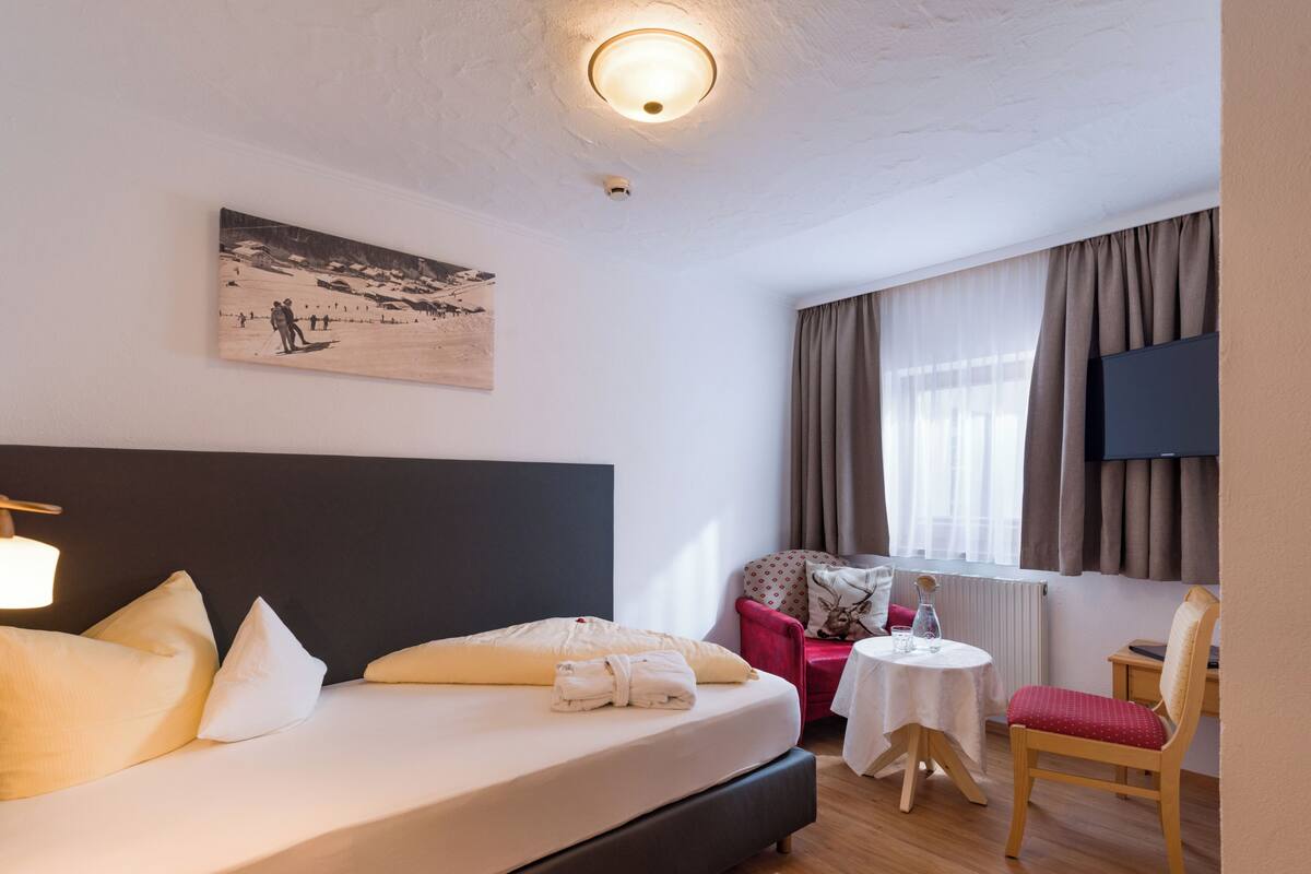 Une chambre d’hôtel avec un lit, une petite table, une chaise, un tableau et un téléviseur.