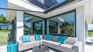Un espacio exterior moderno con un sofá modular, una mesa de vidrio y un taburete redondo pequeño.