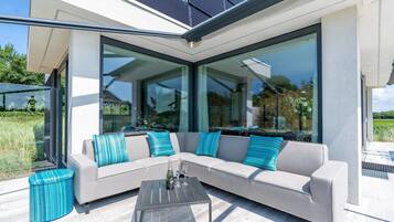Un espacio exterior moderno con un sofá modular, una mesa de vidrio y un taburete redondo pequeño.