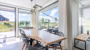Un comedor moderno con una amplia mesa de madera, sillas negras y vistas al exterior a través de grandes ventanales.