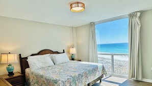 A bedroom with a bed, a nightstand, a lamp, and a view of the beach. - Florida Sunshine Beachfront @ Shoreline Towers 3 br condo with beachfront views (Destin)