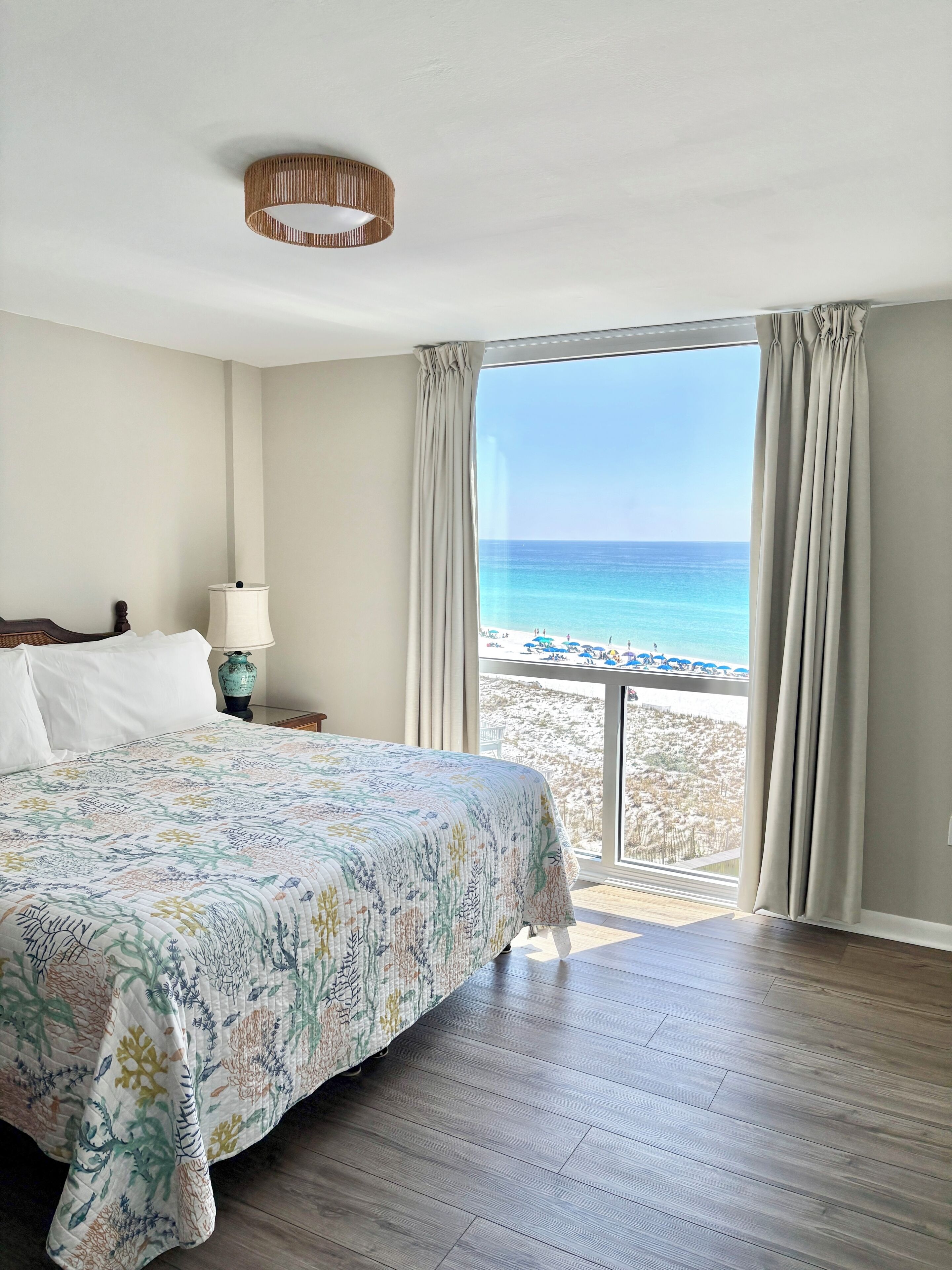 Een hotelkamer met een bed, een lamp, uitzicht op het strand en een balkon.