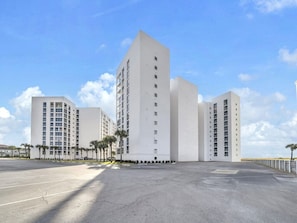 Un bâtiment moderne à plusieurs étages, doté d’un toit plat, entouré d’un parking et de palmiers.