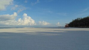 A wide, empty beach with a lifeguard tower and trees in the background.