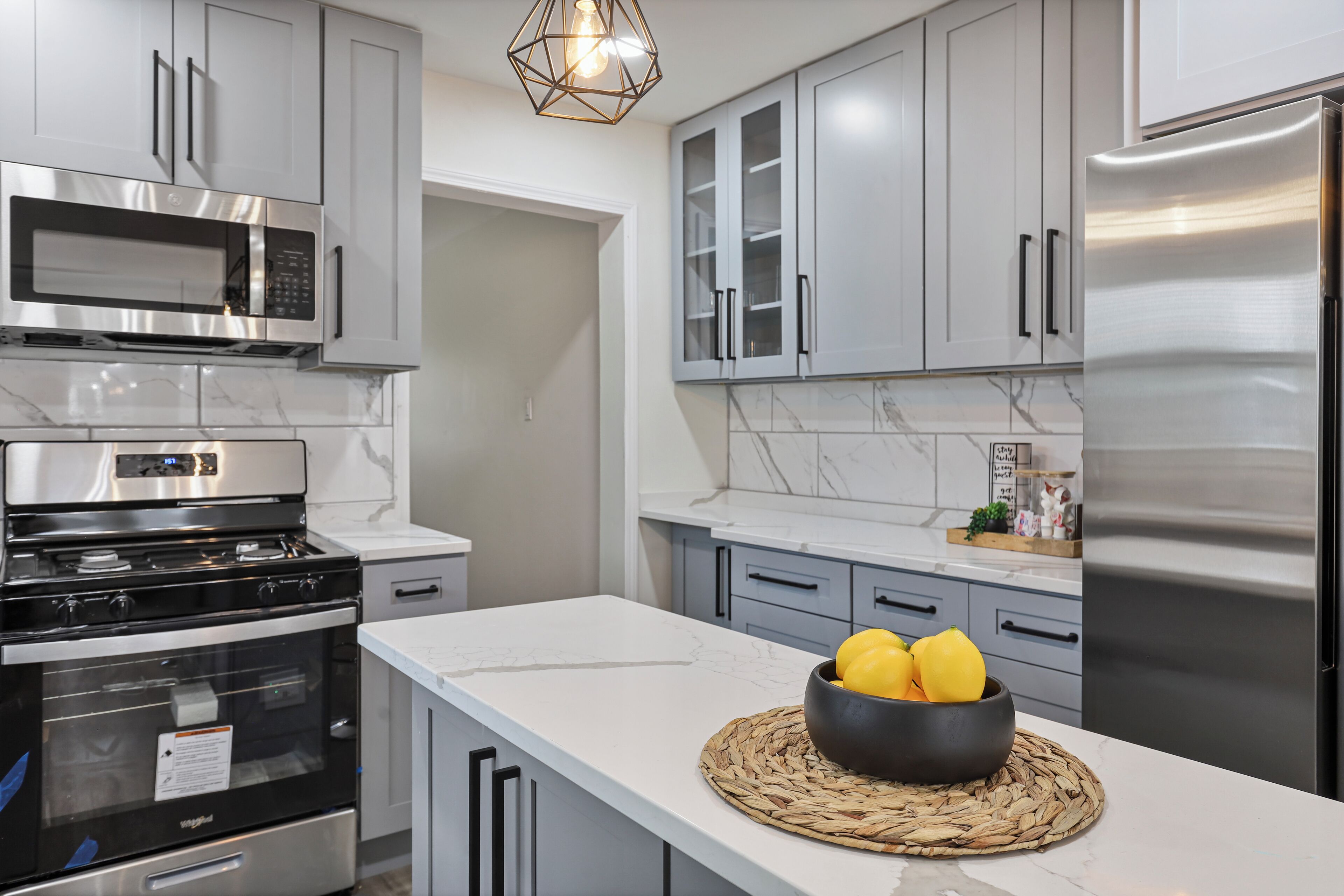 A modern kitchen with stainless steel appliances, grey cabinetry, and a marble backsplash.
